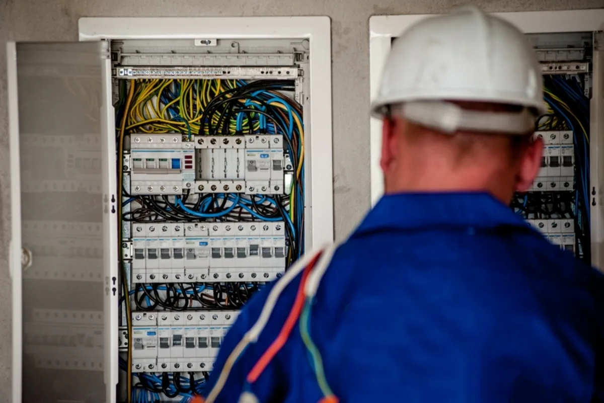 Elektriker mit Schutzhelm arbeitet an einem offenen Zählerschrank