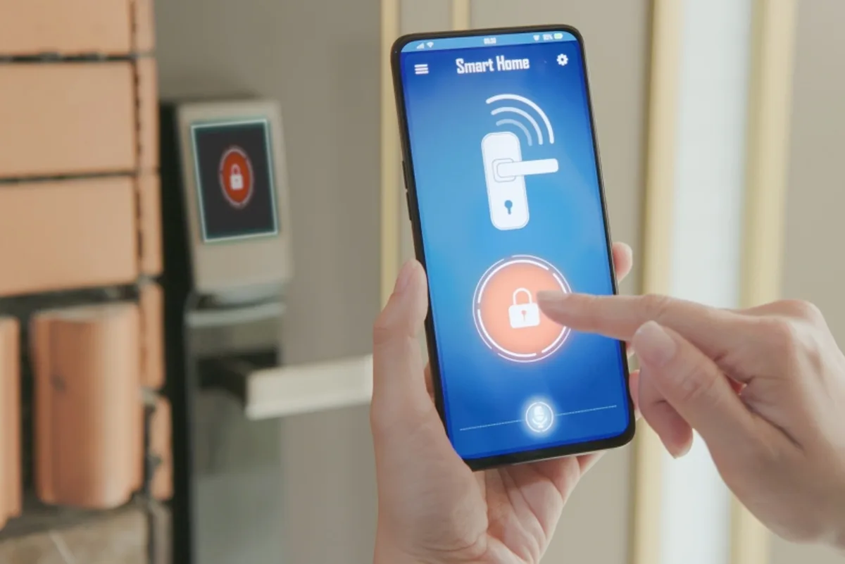 Hand bedient die Türsicherung eines Smart Home über eine App am Smartphone